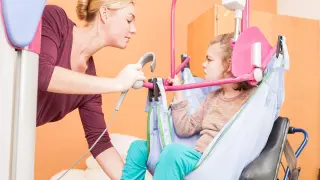 Donna assiste una bambina su un sollevatore, mostrando come sollevare una persona allettata con cura e attenzione.